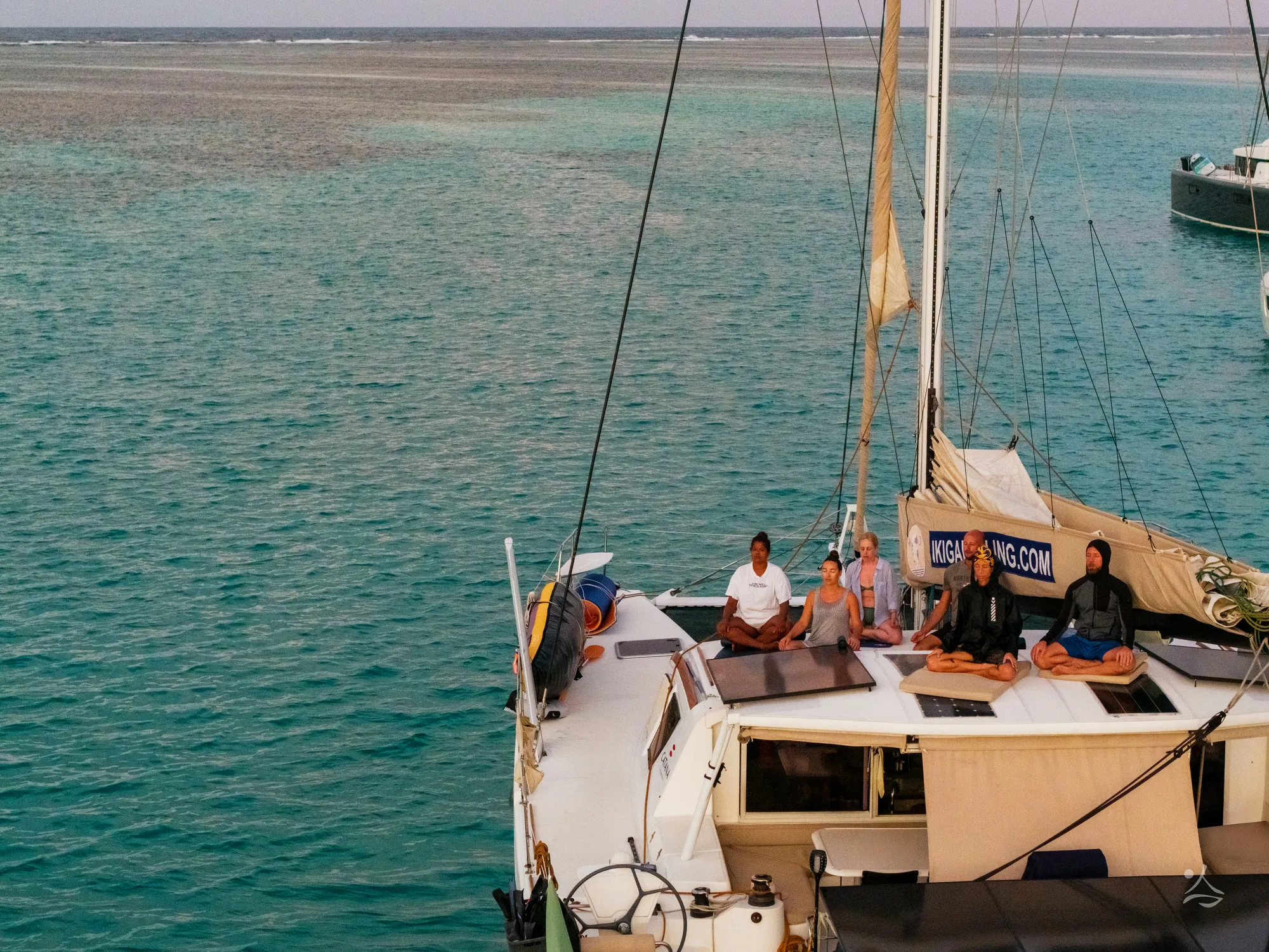 Crew meditating at dawn on the deck of the Ikigai catamaran anchored over a turquoise reef in Guna Yala