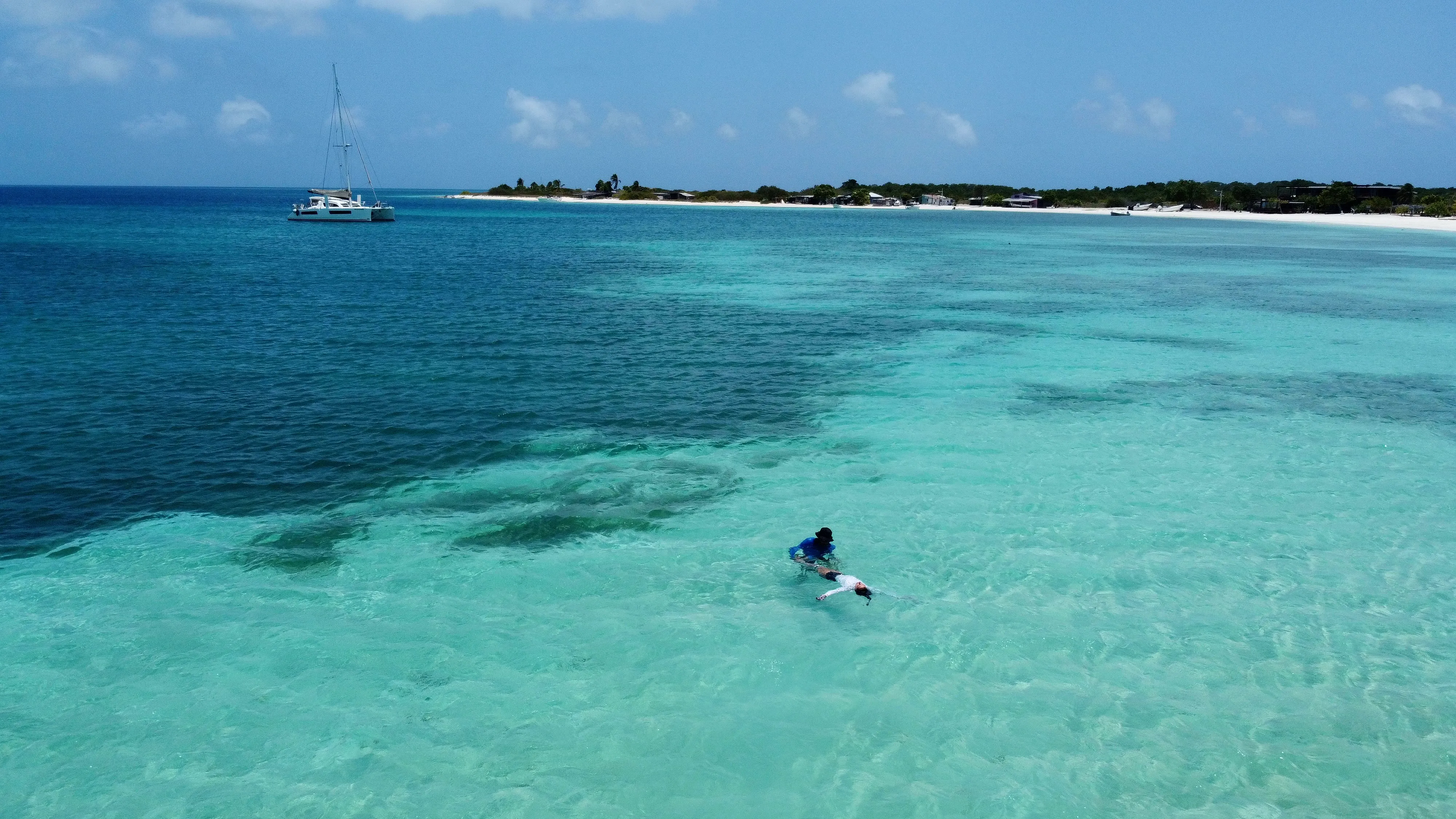 A snorkeler in the shallow turquoise water off a San Blas island, boats at anchor