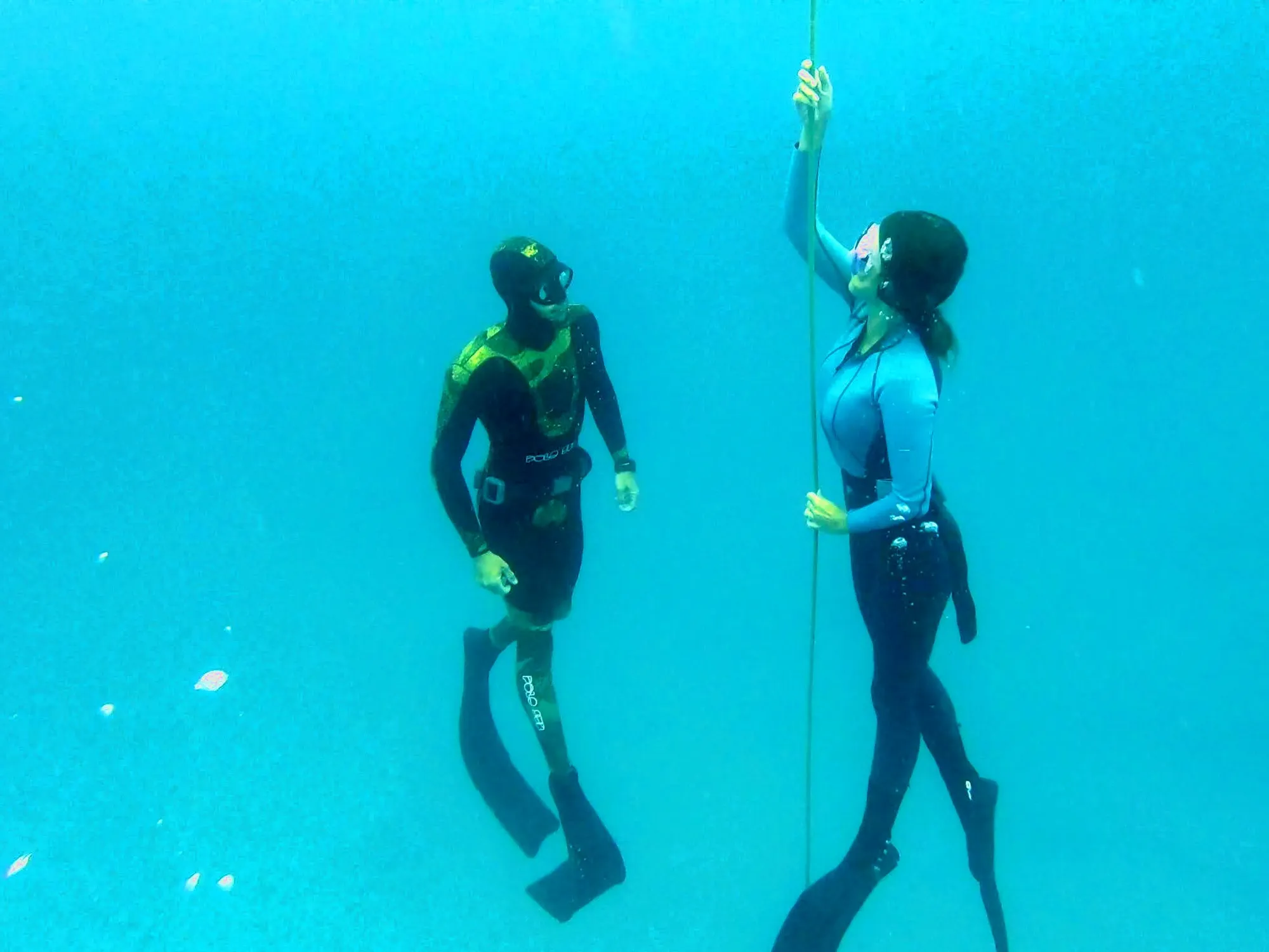 Two freedivers descending along the line in clear turquoise water